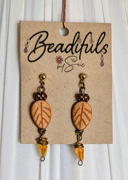Dangle earrings each with one howlite golden leaf and one long amber Bicone bead dangling on antique brass wires with antique brass spacer beads and jump ring accents